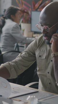 African American man speaking on mobile phone checking information in business document working at desk in office. Communication and job concept.