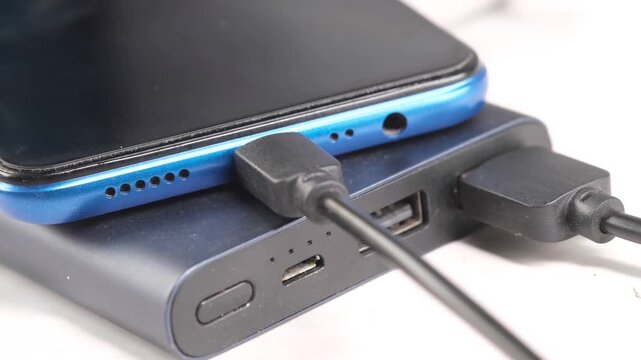 Close up shot of smartphone charging via portable power bank with black usb cable