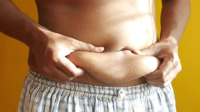 A man's hand pinching his belly fat, emphasizing weight gain and need for a healthy lifestyle, close up motion footage