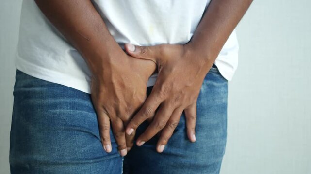 Person holding groin area showing discomfort or pain in jeans