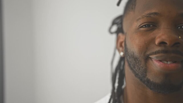 Man smiles showing teeth with earring and beard, dreadlocks visible, closeup portrait in studio; friendly joy.