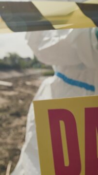 Vertical video of ecologist in hazmat suit cordoning off disaster zone with hazard tape. Footage serves environmental catastrophe reporting, biohazard news, pollution awareness content