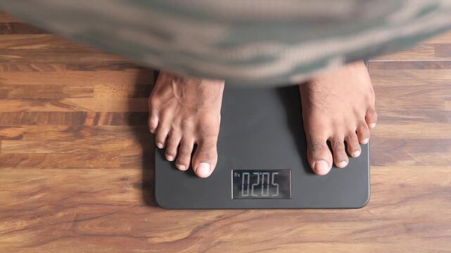 Top view of man standing on digital bathroom scale to measure body weight in kilograms
