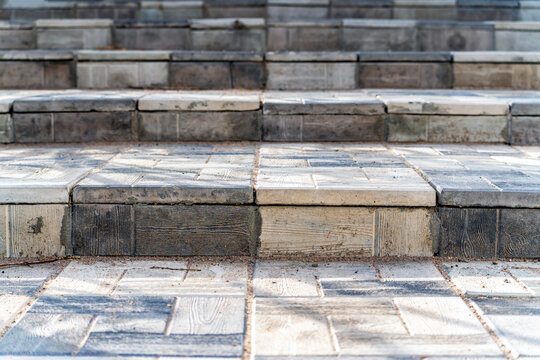 Detailed close-up of outdoor pedestrian steps made of grey and beige concrete paving tiles featuring a realistic faux wood grain texture pattern.