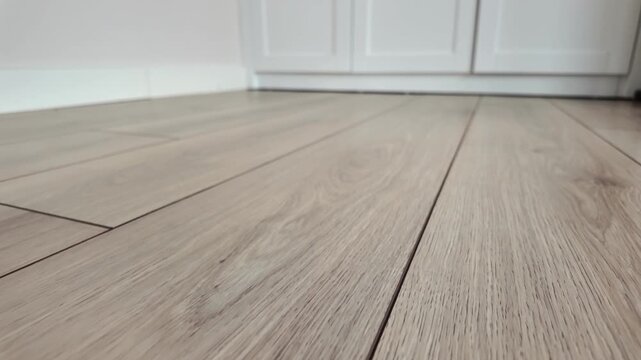 Close up footage of light wood laminate flooring in room near white cabinets and baseboard