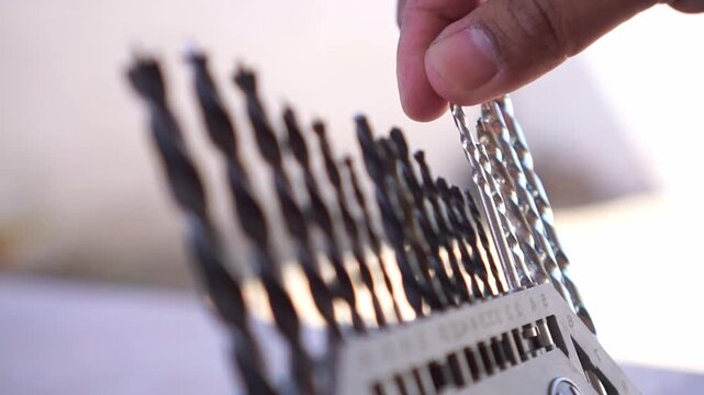 Hand returning drill bit to organizer case, close up shot, various size drill bits, workshop tool storage footage scene.