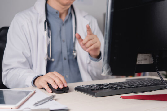 Healthcare professional using desktop computer and pointing at monitor with stethoscope in modern medical office workspace