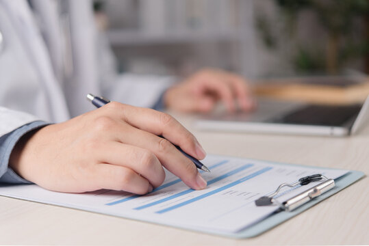 Healthcare professional reviewing bar chart report with pen beside laptop for medical data analysis clinical reporting and administration workflow