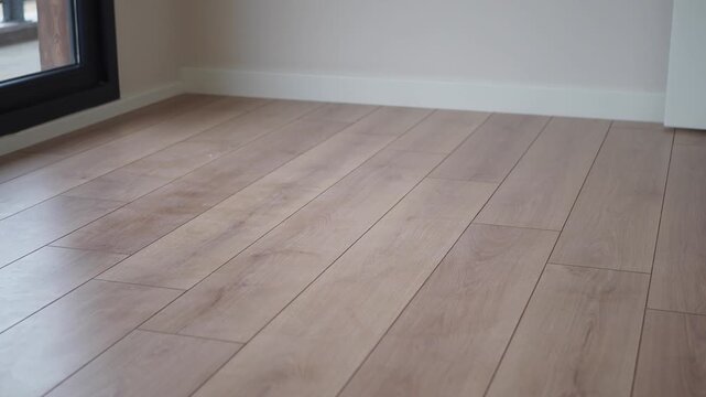 Low angle view of modern light oak laminate flooring in empty room with white baseboards