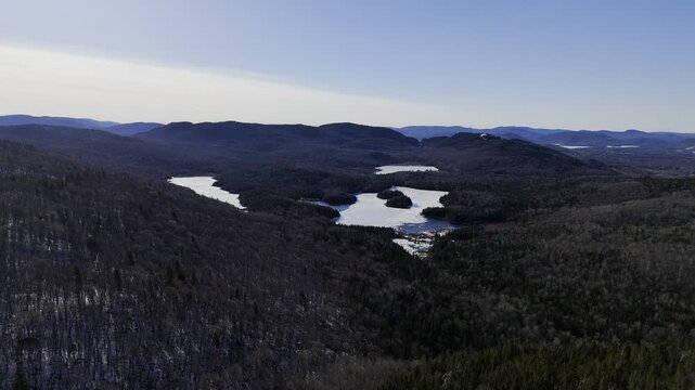 defaultAerial view of winding road along frozen lake in Quebec with forest and mountains under blue sky. g.