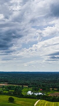 Aerial view of picturesque countryside with rolling green hills and small lake under dramatic cloudy sky.