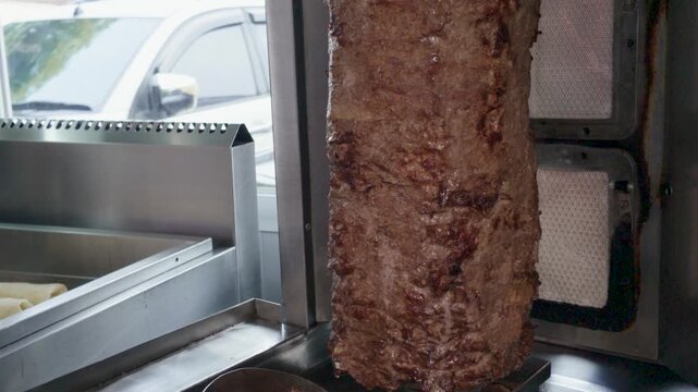 Close-up of traditional meat roasting on a vertical spit rotisserie for doner kebab or shawarma.