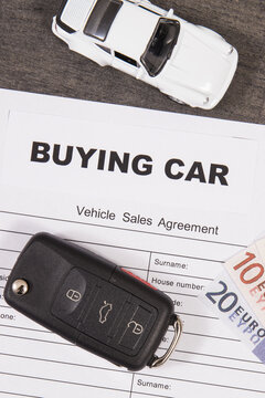 White toy car, car key, euro banknotes and vehicle sales agreement. Inscription buying car. Sales, purchases of automobile. Transportation