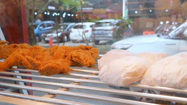 Crispy golden fried chicken and wrapped rice displayed on a food warmer rack at a street restaurant.