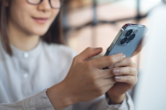 Close up of young asian woman using smartphone browsing internet, checking social media, using mobile app, during working in cafe, modern people lifestyle concept