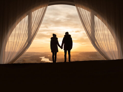Silhouette of a romantic couple holding hands watching a beautiful sunset from a large arched window with flowing curtains transparent background