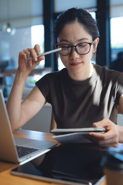 Focused businesswoman remote working, thinking and making a plan in notebook with laptop on table at cafe, thoughtful planning and mobile work concept. vertical