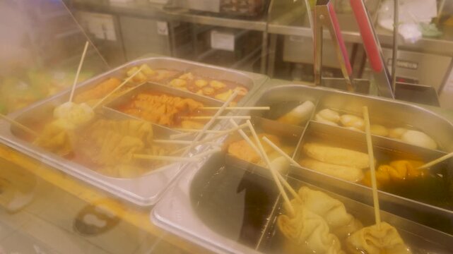 Steaming hot Korean fish cake skewers simmering in savory broth at a street food market counter.