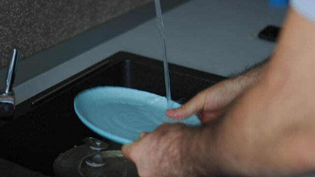 person washing dishes in a modern kitchen sink. Domestic chores, household duties, daily routine, and clean tableware concept with running water and blue plates.