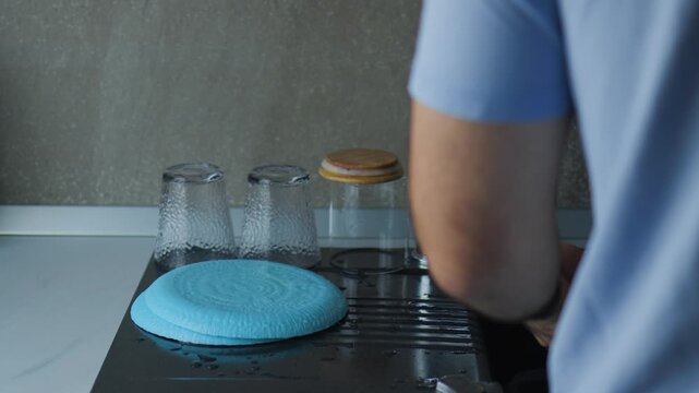 person washing dishes in a modern kitchen sink. Domestic chores, household duties, daily routine, and clean tableware concept with running water and blue plates.