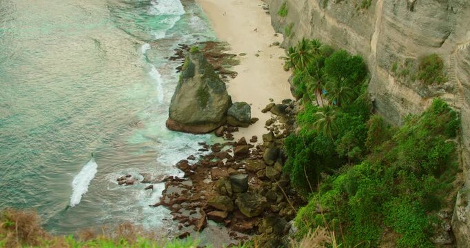 White sand beach meets turquoise ocean water at base of steep coastal cliffs in Nusa Penida Island Bali