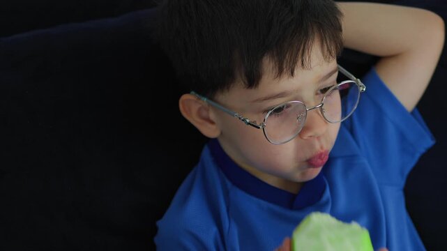 cute young boy with glasses eating a fresh green apple. Healthy childhood nutrition, daily vitamin snack, and casual indoor lifestyle portrait of a kid enjoying organic fruit.