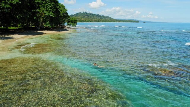 Woman swimming along coral reef near sandy beach under bright summer sun in Costa Rica