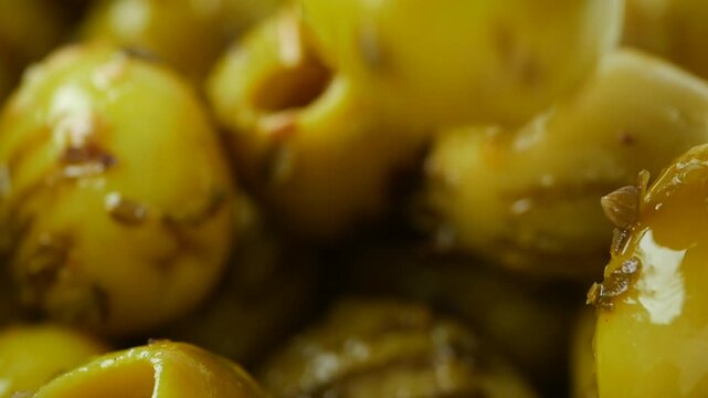 Close up slow motion video of a fork picking up green marinated olive, revealing textured surface and glistening oil, fresh and juicy olives, macro view footage