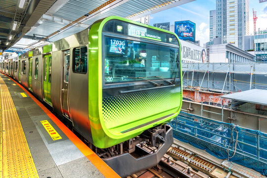 Green commuter train arrives at railway platform in Shibuya Tokyo Japan