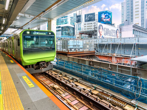 Green commuter train arrives at railway platform in Shibuya Tokyo Japan