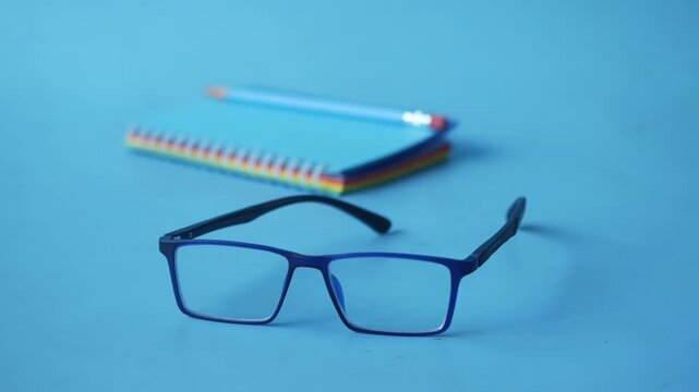 A close up view of blue-framed eyeglasses with colorful notepads and a pen in the background, creating a calm and focused atmosphere suitable for study or work settings