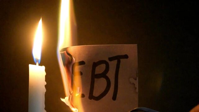 Lit candle. Fire burning a piece of paper with the word debt handwritten on it. Symbolic act, gesture.