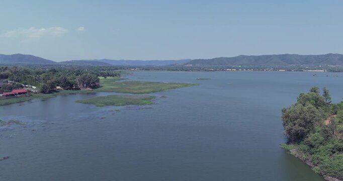 Backward aerial view of a serene lake nestled between lush, forested hills on a bright, clear day.