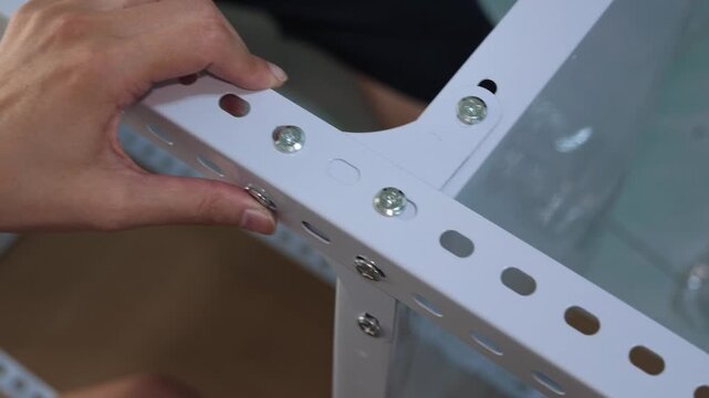 Close up of hands fitting a white steel shelf bracket during DIY furniture assembly at home