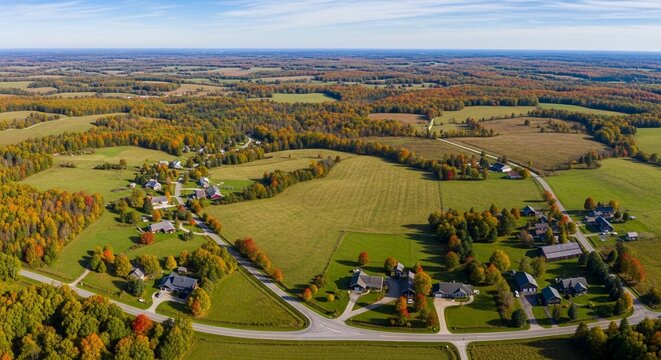 Expansive Autumn Aerial View of a Suburban Neighborhood Nestled Within Rolling Countryside Fields and Colorful Trees