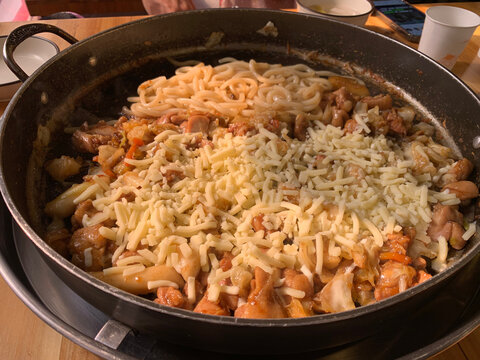 Spicy Korean dak galbi with chicken, cabbage, rice cake and melted cheese cooks in a large black pan at a restaurant in Gapyeong, South Korea
