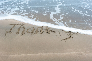 Fototapeta premium Thanks handwritten on sand with ocean water wave background.