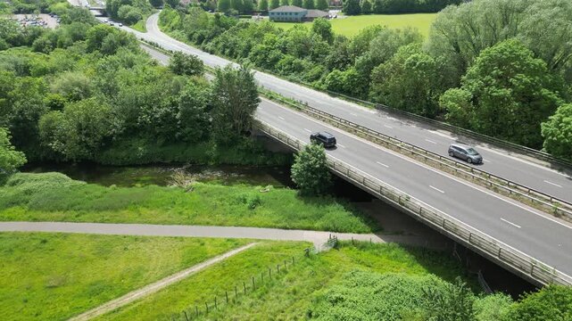Aerial view of cars traveling along motorway bridge crossing small river in rural countryside.