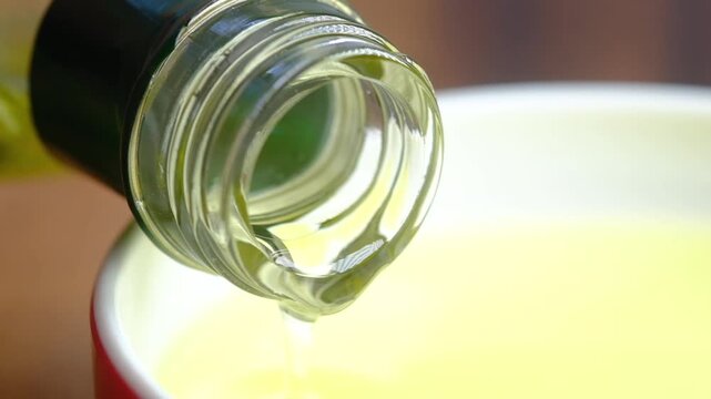Slow motion pouring of extra virgin olive oil from bottle into bowl