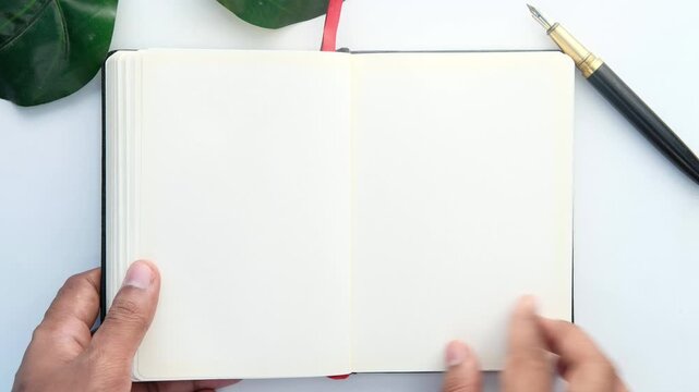 Hands flipping through empty pages of blank journal diary with fountain pen and green leaf on white background