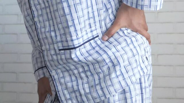 Unrecognized man wearing striped pajamas holding his back while suffering from chronic lower lumbar pain
