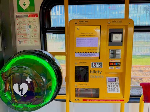 Modern yellow self-service ticket vending machine with BLIK and Visa payment options alongside a green Philips AED defibrillator inside a Polish city tram
