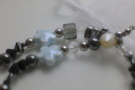 Handmade accessory pieces featuring light blue floral charms and metallic beads arranged on a clean white surface to display intricate jewelry design details