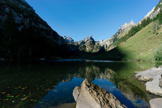 Serene view of Seealpsee lake reflecting the majestic peaks of the Alpstein massif in the Appenzell Alps, Switzerland, with rocks in the foreground