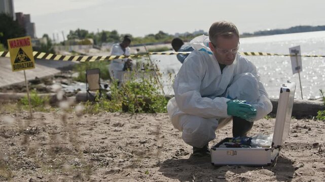 Caucasian middle aged scientist in hazmat suit examining contaminated soil samples near biohazard zone. Clip suitable for ecological disaster documentaries and environmental hazard reports