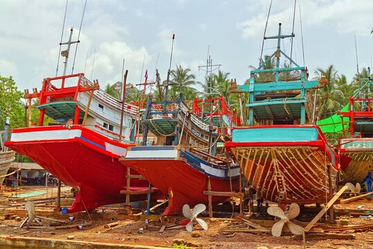 Traditional colorful wooden Thai fishing boats undergoing maintenance and repairs on dry land along the coast in Sichon, Nakhon Si Thammarat province, Thailand.