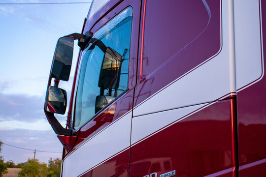 Close-up of a modern red semi-truck cab with side mirrors and white graphic stripes. Ideal for heavy transport, commercial fleet, freight delivery, and logistics concepts.