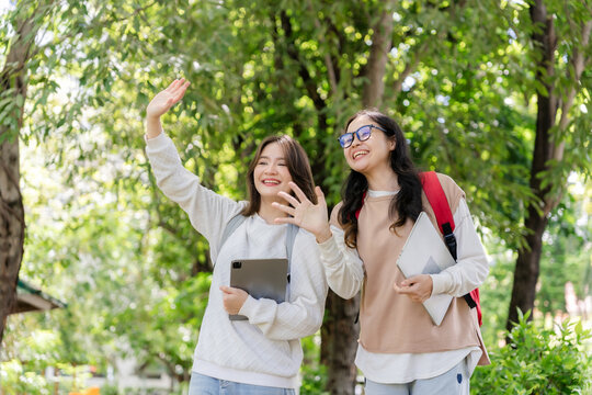 Group of student friends wearing backpacks smiling and waving hands excitedly together on university campus.