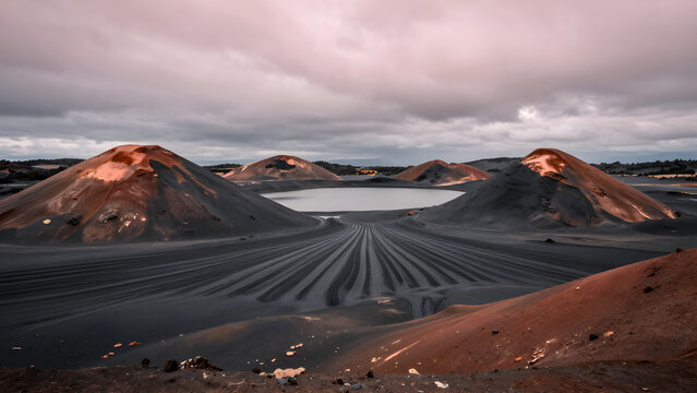 Volcanic landscape with dark sand and distant hills under cloudy sky