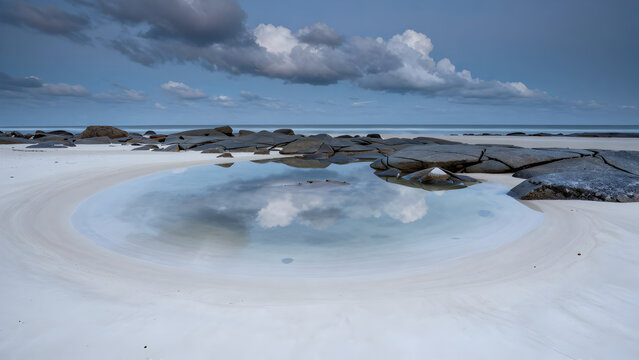 Tidal pool reflection on a wide sandy beach under cloudy sky